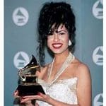 Selena Quintanilla posando en la ceremonia de los premios Grammy, sosteniendo su Grammy, con un vestido brillante y su icónico peinado alto y voluminoso