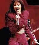 Selena Quintanilla actuando en el escenario, vistiendo un conjunto rojo brillante y cantando con energía, mostrando su carisma en un concierto en los años 90