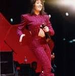 Selena Quintanilla en pleno concierto, bailando y cantando con energía, vestida con un conjunto rojo brillante, reflejando su estilo vibrante y carismático.