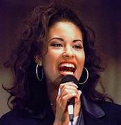 La voz de Selena: Un legado musical inolvidable.Selena Quintanilla cantando al micrófono en el escenario, con un peinado voluminoso, grandes aros y transmitiendo emoción y energía mientras se presenta