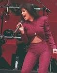 Selena Quintanilla actuando en el escenario con un conjunto morado, cantando y transmitiendo energía y emoción durante su presentación en vivo