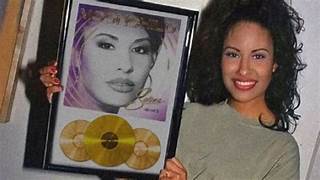 Selena Quintanilla sostiene un reconocimiento enmarcado con discos de oro, como parte de su exitosa discografía.